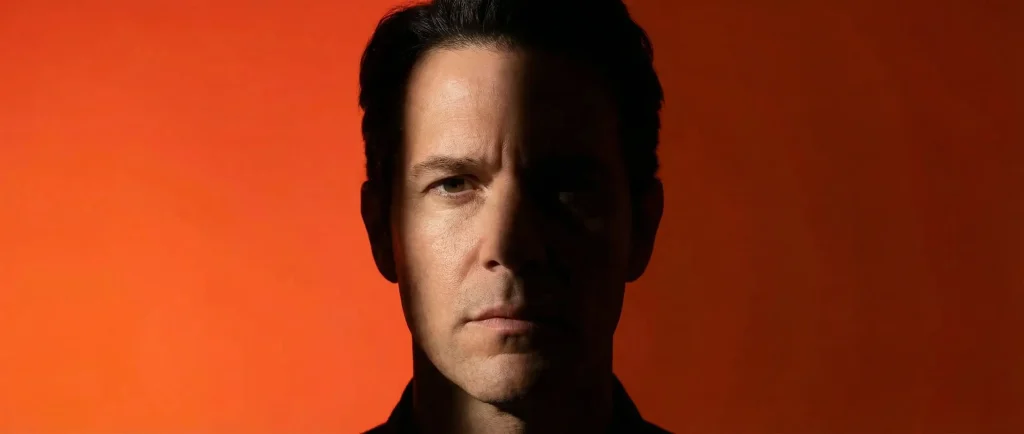 Портрет чоловіка з напівосвітленим обличчям на темному помаранчевому фоні